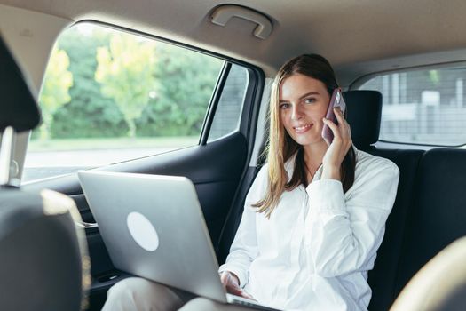 Beautiful female passenger car works on a laptop and uses a mobile phone