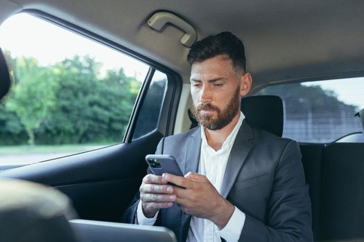 Happy and successful male businessman car passenger reads the news from the phone, rejoices in the victory and the news received