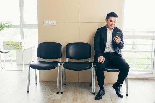 Male asian businessman got good news, rejoices in the waiting room for an interview, near the reception of a modern business center