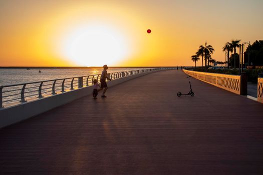 Children playing with balloon on boardwalk during sunset hour. Outdoors.