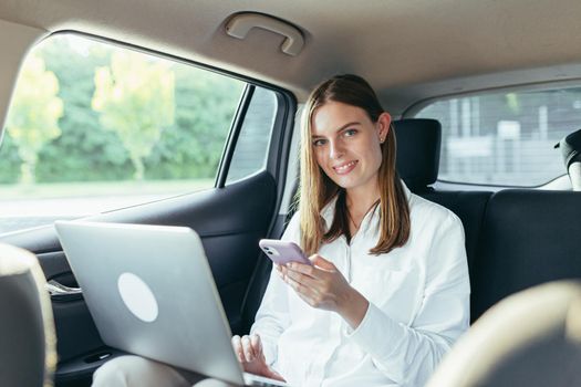 Beautiful female passenger car works on a laptop and uses a mobile phone