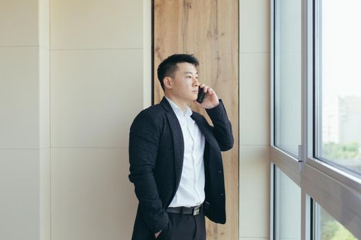 serious boss asian businessman talking on the phone in a modern office center, makes a working call to colleagues