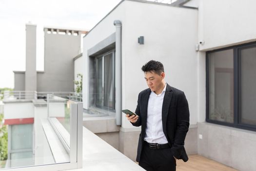 Freelancer Asian businessman in business suit enjoys phone standing on balcony terrace of modern office center