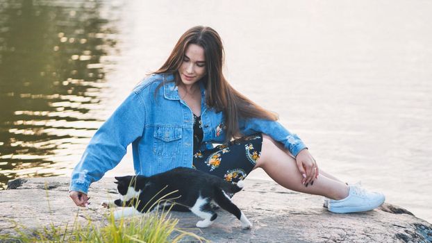 A girl plays with a cat by the lake