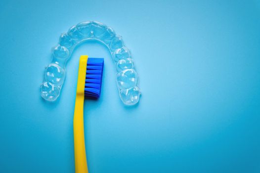 a bright toothbrush in yellow with plastic new braces lies on a blue background, no people.