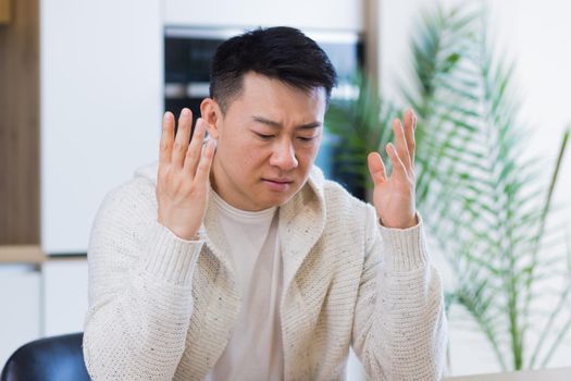 Thoughtful serious young asian man looking away. student writer sit at home office desk with laptop thinking of inspiration search solution ideas lost in thoughts dreaming solving financial problems