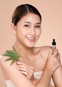 Closeup young ardent woman with healthy fresh skin holding green hemp leaf and cbd oil. Combination of beauty and cannabis concept.