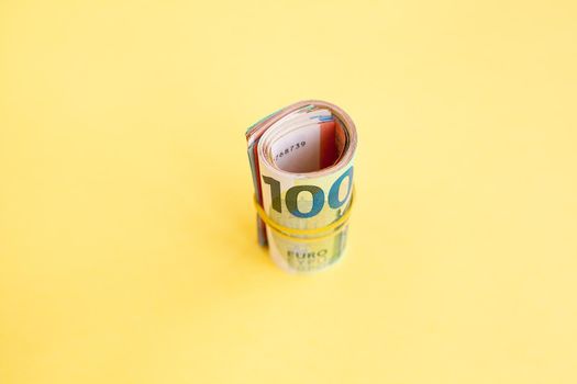 Money roll of euro banknotes with yellow rubber band on yellow background. cash paper currency, payment, earning and savings, european currency, money and finance concept. Empty space for text