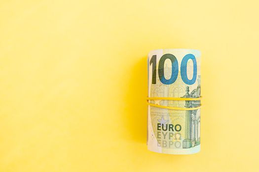 Money roll of euro banknotes with yellow rubber band on yellow background. cash paper currency, payment, earning and savings, european currency, money and finance concept. Empty space for text