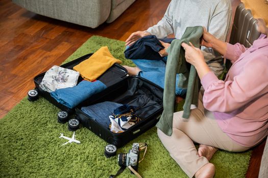 Asian couple old senior marry retired couple prepare luggage suitcase arranging for travel, Romantic retired couple packing clothes travel bag suitcase together on floor at home interior living room