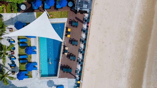 Aerial view from above at pool, tropical swimming pool from above with a drone. Men and women relaxing at a luxury pool during a honeymoon