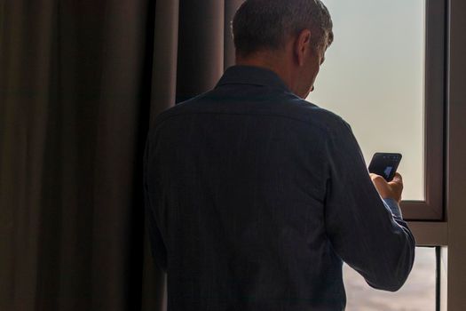 Silhouette of a man with mobile phone at the window