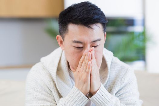 young asian man sitting on sofa at home pensive, worried about problems and depression. male has an experience relationships at work or family, problems with loan repayment debt Seriously conceived