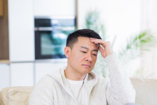 Bored friends young asian man sitting on sofa at home alone. Misses male sitting on the couch in apartment. Lonely guy indoors living room. Worried and stressed about problems in the family or at work