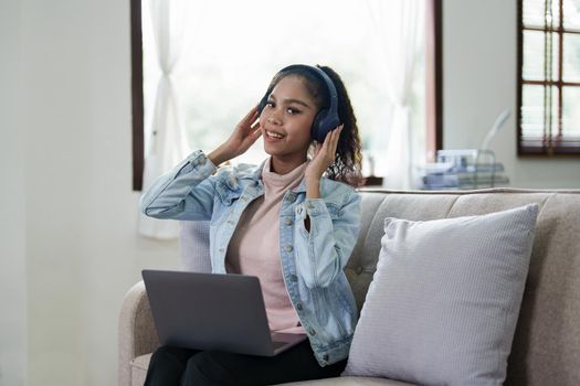 Portrait of an African American sitting on the sofa wearing on-ear headphones and using a computer at home.