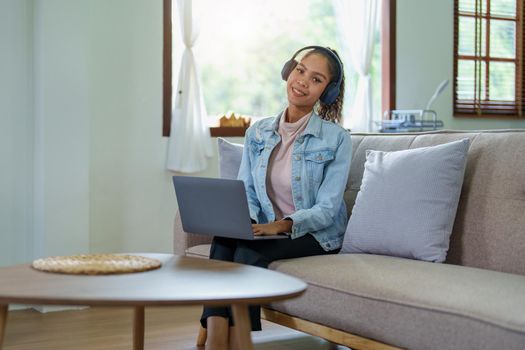 Portrait of an African American sitting on the sofa wearing on-ear headphones and using a computer at home.