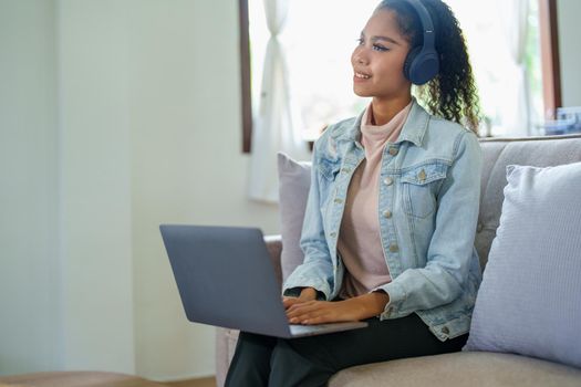 Portrait of an African American sitting on the sofa wearing on-ear headphones and using a computer at home.