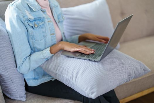 African American sits on the sofa and works on the computer at home.