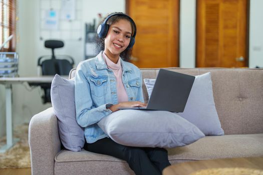 Portrait of an African American sitting on the sofa wearing on-ear headphones and using a computer at home.