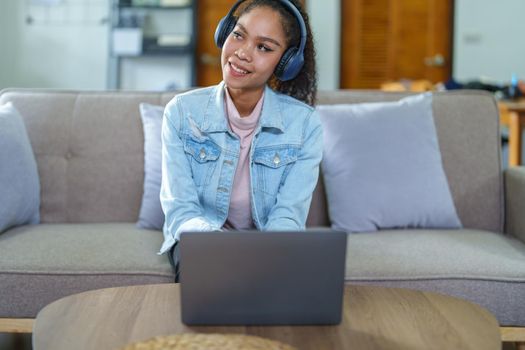 Portrait of an African American sitting on the sofa wearing on-ear headphones and using a computer at home.