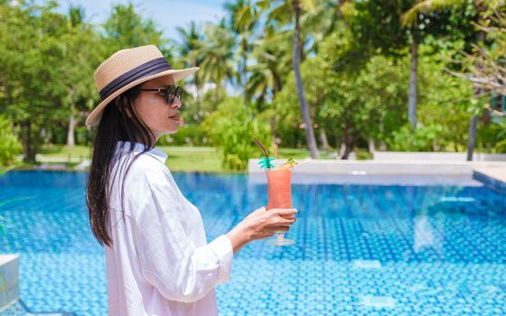 Asian women with a colorful mocktails at a pool bar, orange and green cocktails by the pool of a luxury resort in Thailand