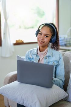 Portrait of an African American sitting on the sofa wearing on-ear headphones and using a computer at home.