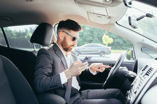 Male businessman sitting behind the wheel of a car, frustrated can not understand the steering and instructions funky car, reads additional information from the phone