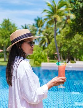 Asian women with a colorful mocktails at a pool bar, orange and green cocktails by the pool of a luxury resort in Thailand