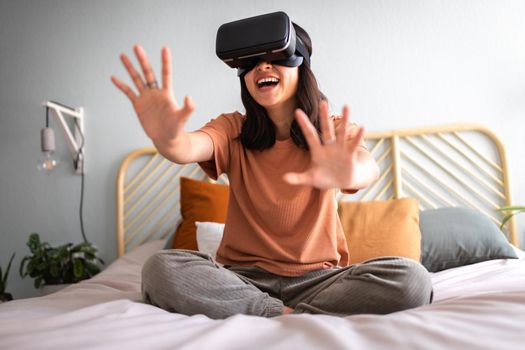 Happy young asian woman at home moving hands playing simulation video game in virtual reality using VR goggles. Modern technology and entertainment.