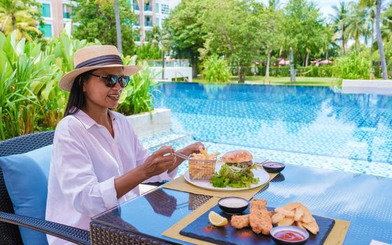 Asian women having lunch by the pool with hamburgers and fish and chips.