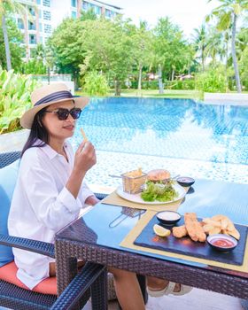 Asian women having lunch by the pool with hamburgers and fish and chips.