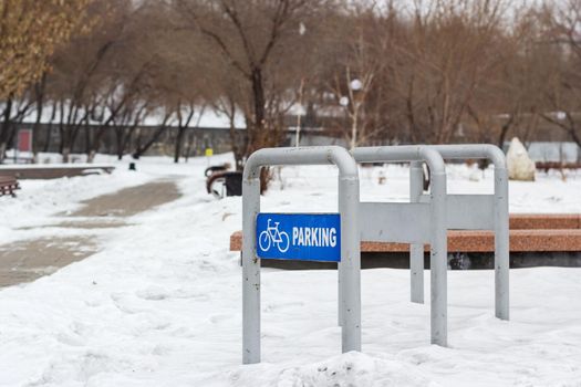 Empty bike parking in snowy public park at cold white winter, urban bicycle station in city recreation zone with cloudy weather