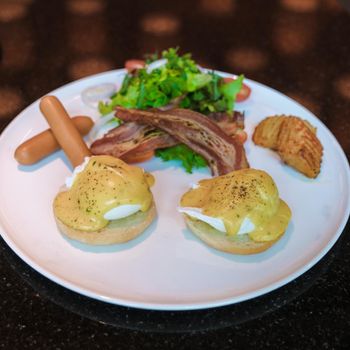 Egg benedict isolated on a plate with salad and sausage and cream hollandaise sauce