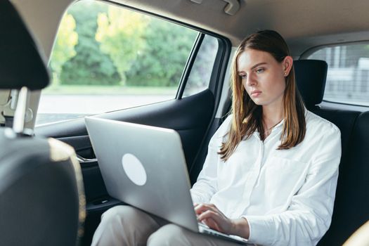 Beautiful female passenger car works on a laptop and uses a mobile phone