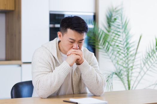Thoughtful serious young asian man looking away. student writer sit at home office desk with laptop thinking of inspiration search solution ideas lost in thoughts dreaming solving financial problems