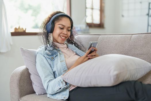 Portrait of an African American sitting on a sofa using a phone and wearing headphones to relax.
