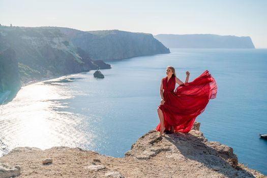 A woman in a red flying dress fluttering in the wind, against the backdrop of the sea