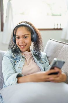 Portrait of an African American sitting on a sofa using a phone and wearing headphones to relax.
