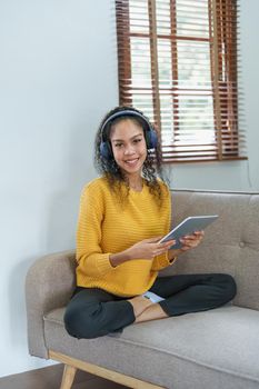 Portrait of an African American sitting on a sofa using tablet and wearing headphones to relax.
