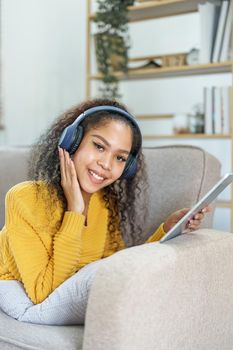 Portrait of an African American sitting on a sofa using tablet and wearing headphones to relax.