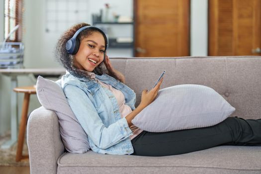 Portrait of an African American sitting on a sofa using a phone and wearing headphones to relax.