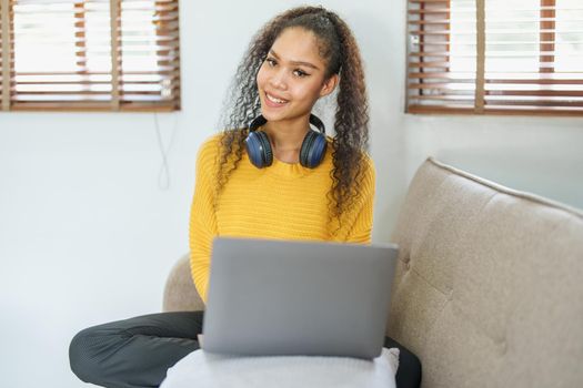 Portrait of an African American sitting on the sofa wearing on-ear headphones and using a computer at home.