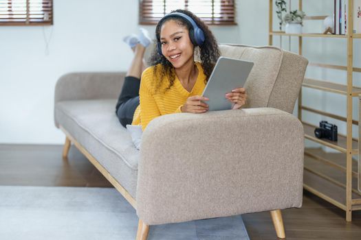 Portrait of an African American sitting on a sofa using tablet and wearing headphones to relax.