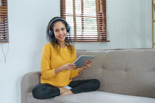 Portrait of an African American sitting on a sofa using tablet and wearing headphones to relax.