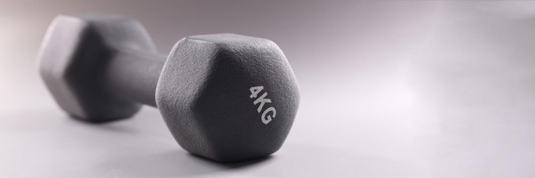 Black sports dumbbell for bodybuilding on gray background closeup. Sale of sports accessories concept