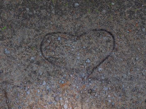 Heart in love painted with a stick in dry needles and dry clay. Dry soil in forest path