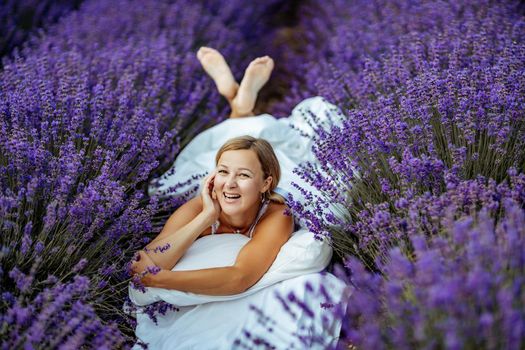 A middle-aged woman lies in a lavender field and enjoys aromatherapy. Aromatherapy concept, lavender oil, photo session in lavender.
