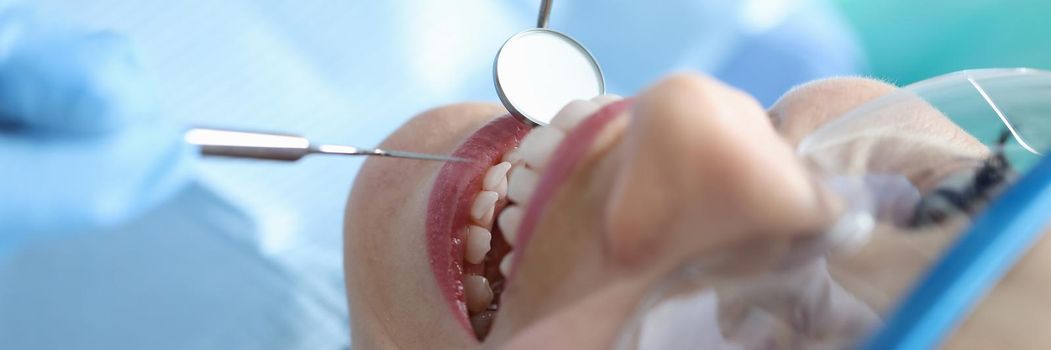 Dentist examining oral cavity of woman patient in clinic using tools closeup. Annual dental checkups concept