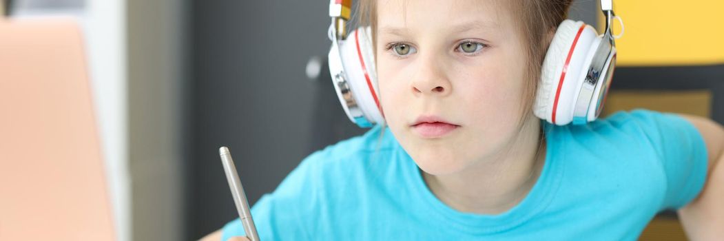 Little girl schoolgirl in headphones sitting in front of laptop at home. Homeschooling concept