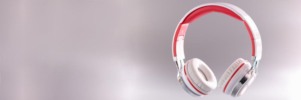 Closeup of red and white wireless headphones on gray background. Modern music listening accessories concept